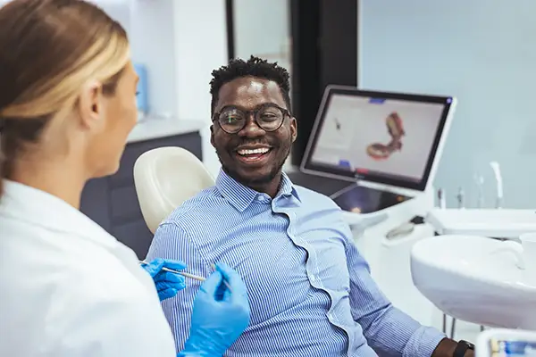 A male patient smiling and interacting with a dentist during a consultation, with advanced dental imaging equipment visible in the background.
